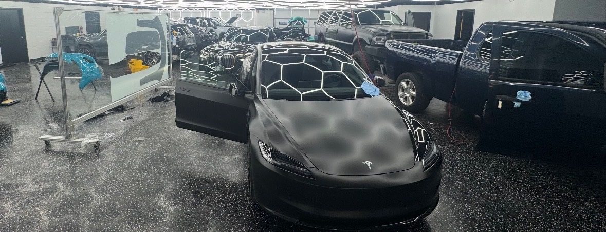Tesla Model 3 matte black wrap in busy install bay — Sleepr Studio College Station TX